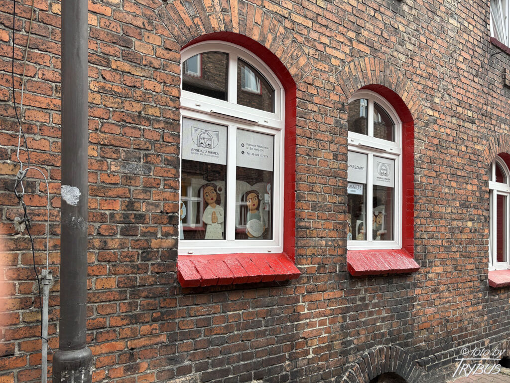 Fotografia przedstawia typowe okna na osiedlu Nikiszowiec w Katowicach – z białą stolarką i czerwonym obramowaniem łącznie z parapetem. Powstało w latach 1908-1924 dla górników kopalni „Giesche” z inicjatywy koncernu górniczo-hutniczego „Georg von Giesches Erben”.