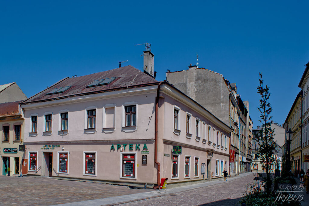 Fotografia przedstawia południowo-wschodnie naroże Starego Rynku w Białej Krakowskiej (obecnie to plac Wojska Polskiego w Bielsku-Białej). Mieści się tu apteka Pod Białym Orłem – to najstarsza bialska apteka założona w 1701 r.